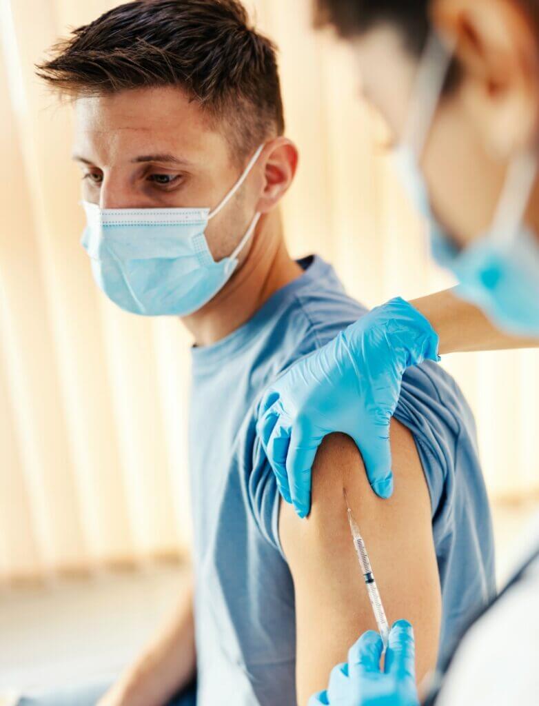 Patient wearing mask receiving shot from healthcare provider or nurse